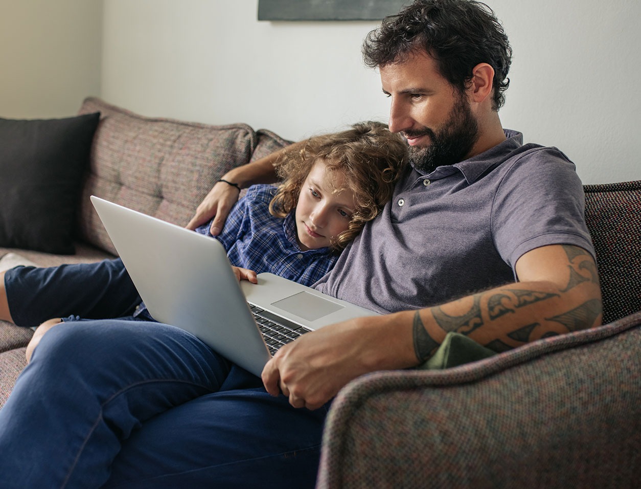 Dad on laptop while sitting on the couch with kid